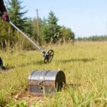 Person metal detecting in a grassy field with trees.