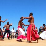 Diverse people practicing Capoeira outdoors in traditional attire.