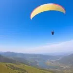 Paraglider flying over green hills and a river.