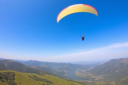 Paraglider flying over green hills and a river.